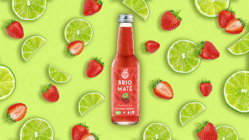 Présentation de la bouteille Brio Maté Strawberry & Lime sur un fond vert avec des fraises et des limes